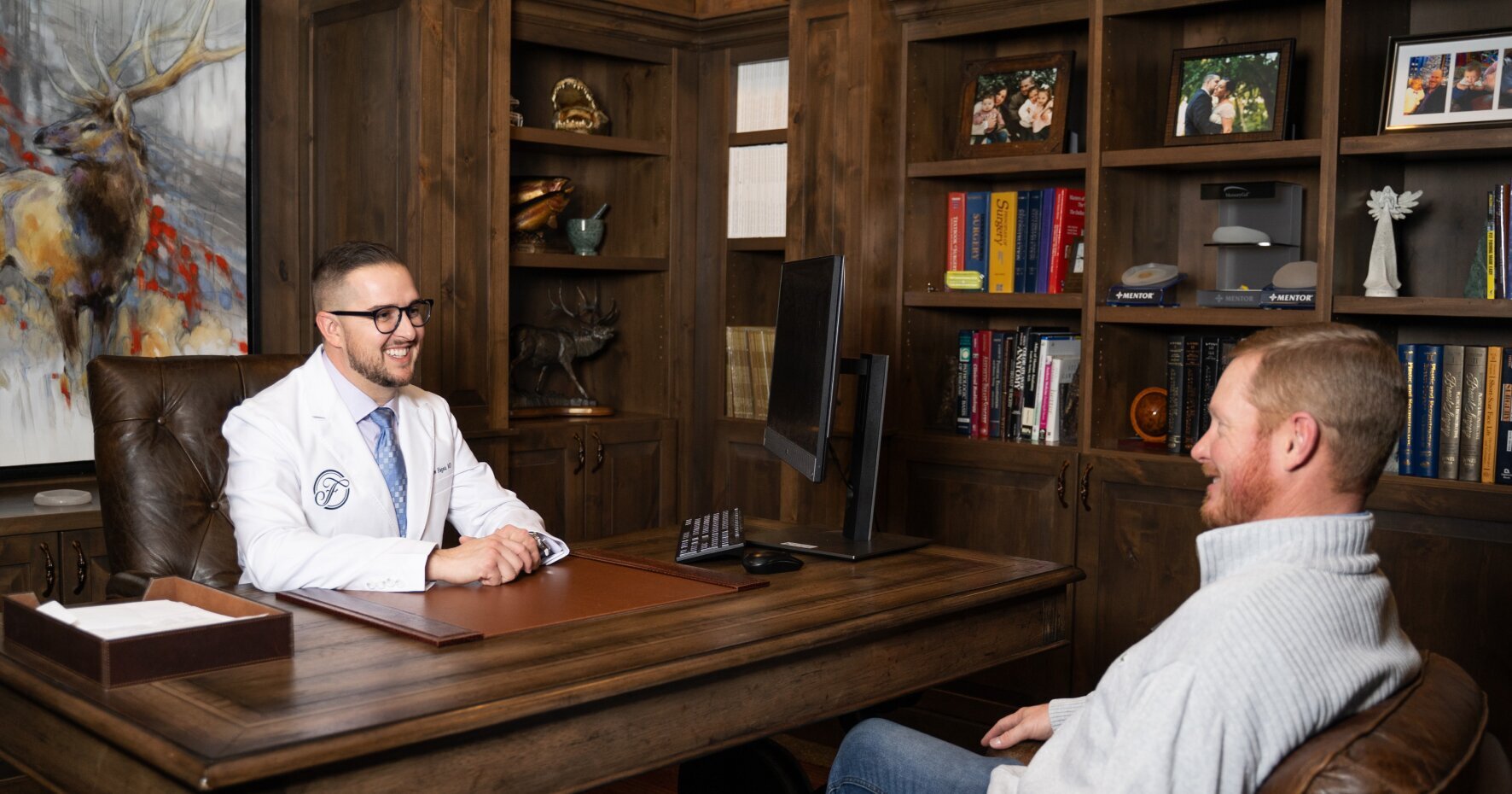 Reading Plastic Surgeon Dr. Matthew Hagan sitting at desk while talking with patient